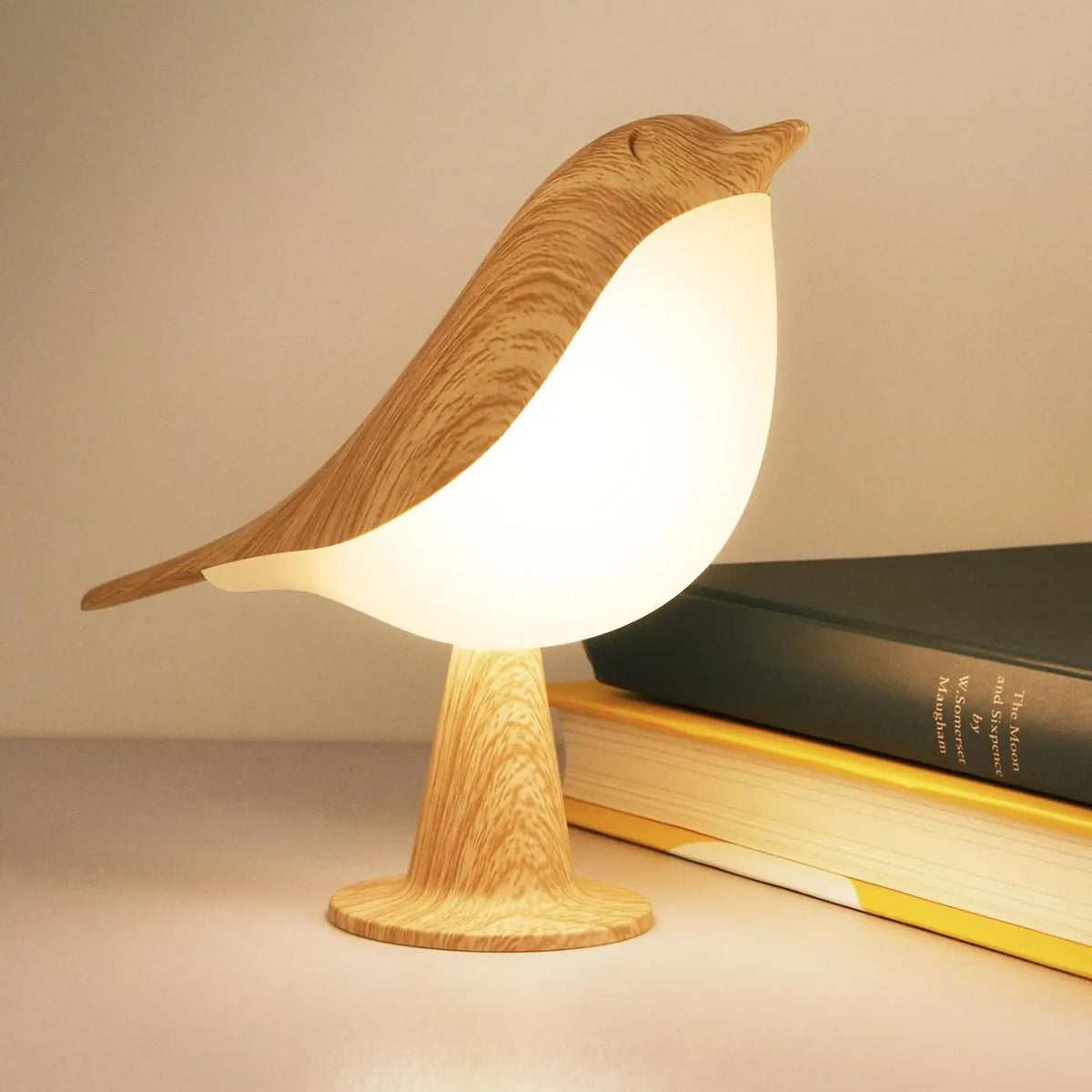 Leuchtende Vogellampe mit Holzmaserung steht auf einem Tisch neben zwei aufeinanderliegenden Büchern 1