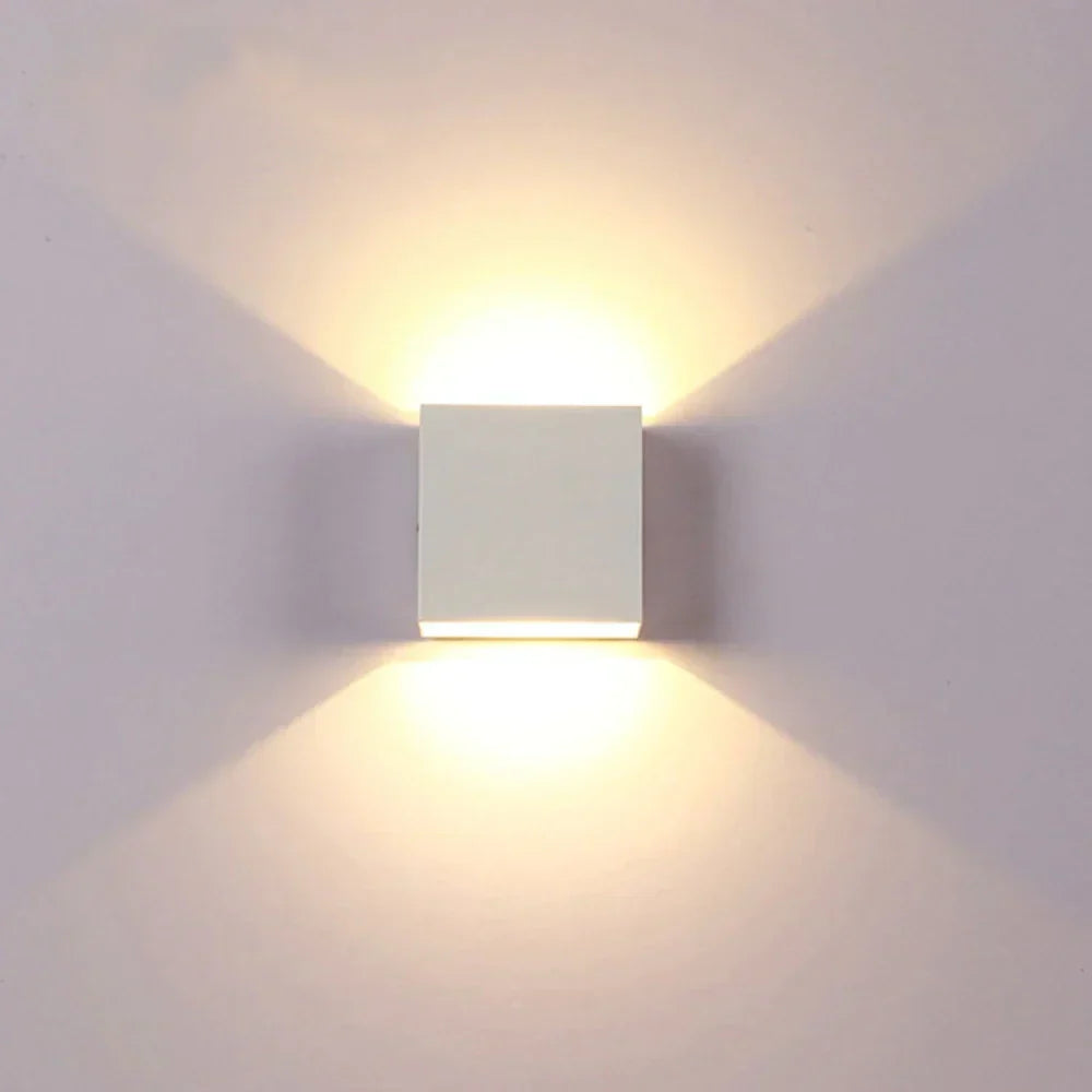 Weiße Würfelleuchte frontal an heller Wand, Licht strahlt nach oben und unten in warmem Ton. 17