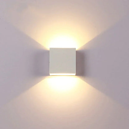 Weiße Würfelleuchte frontal an heller Wand, Licht strahlt nach oben und unten in warmem Ton. 17
