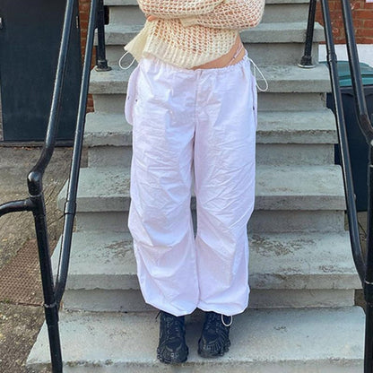 Frau in weißer Cargohose und Strickpullover auf Treppe, modische Freizeitkleidung.