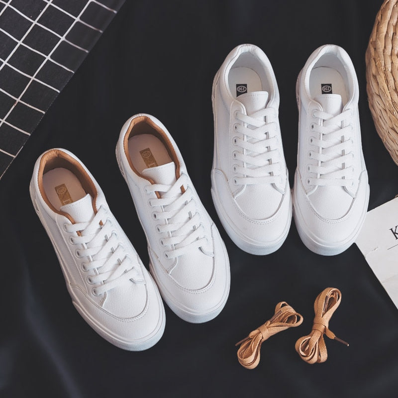 Weiße Sneaker aus Leder, Unisex, mit braunen Schnürsenkeln, auf schwarzem Hintergrund.