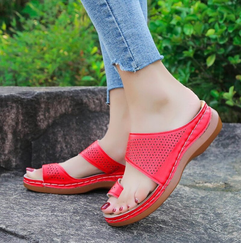 Rote Damen-Sandalen, bequem, mit Keilabsatz, Sommermode, auf Steinweg, grüne Hintergrund.