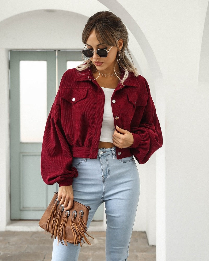 Frau in roter Cordjacke, blauer Jeans, Sonnenbrille, mit brauner Fransenhandtasche.