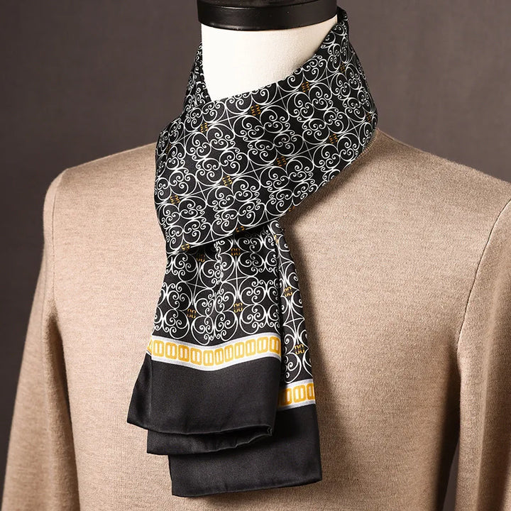 Schwarzer Schal mit weißem Schnörkelmuster und gelber Bordüre, um den Hals einer Büste über einem beigen Pullover drapiert. 25