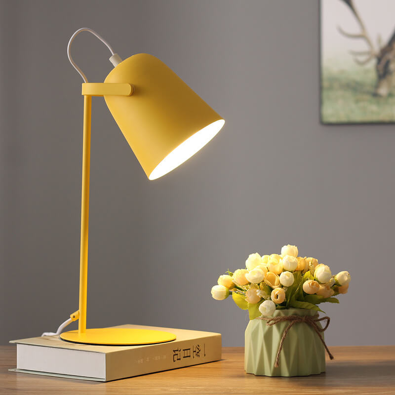 Gelbe Tischlampe auf einem Buch, eingeschaltet, mit Blumenvase auf dem Holztisch und einem Bild an der grauen Wand. 7