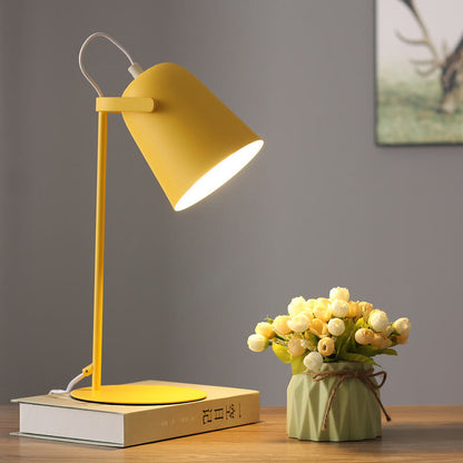 Gelbe Tischlampe auf einem Buch, eingeschaltet, mit Blumenvase auf dem Holztisch und einem Bild an der grauen Wand. 7