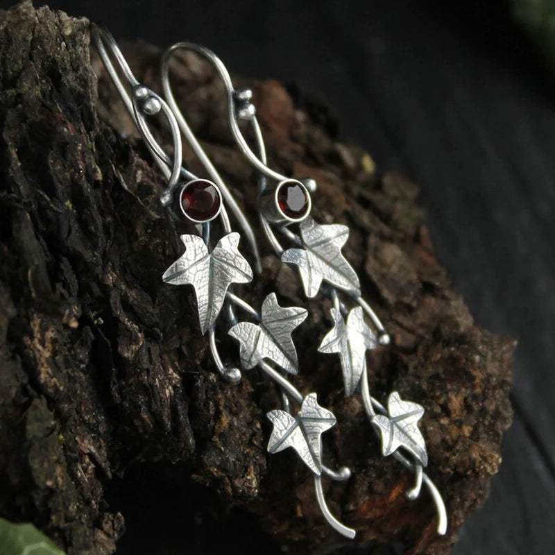 Silberne Ohrringe mit Efeublatt-Design und roten Steinen auf Holz, handgefertigter Schmuck.