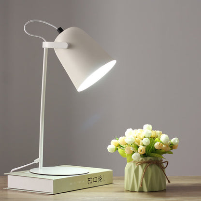 Weiße Tischlampe mit hellem Licht auf einem Buch, daneben eine Vase mit hellen Röschen auf dem Holztisch. 11