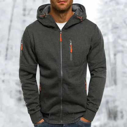 Mann trägt den dunkelgrauen Kapuzenpullover mit orangefarbenen Zippern, aufgesetzter Brusttasche und Rippbündchen vor verschneitem Wald. 9