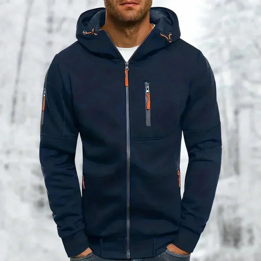 Mann trägt den marineblauen Kapuzenpullover mit orangefarbenen Zippern an Brust, Ärmel und Seitentaschen vor Schneehintergrund. 5