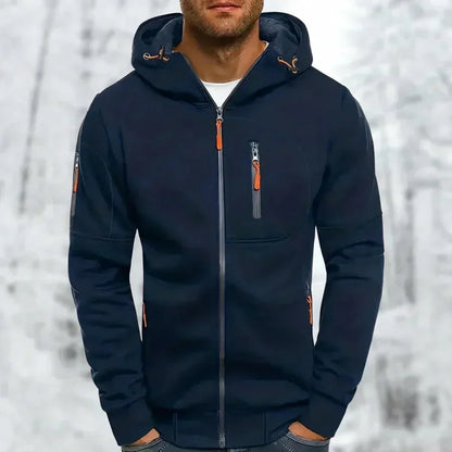 Mann trägt den marineblauen Kapuzenpullover mit orangefarbenen Zippern an Brust, Ärmel und Seitentaschen vor Schneehintergrund. 5