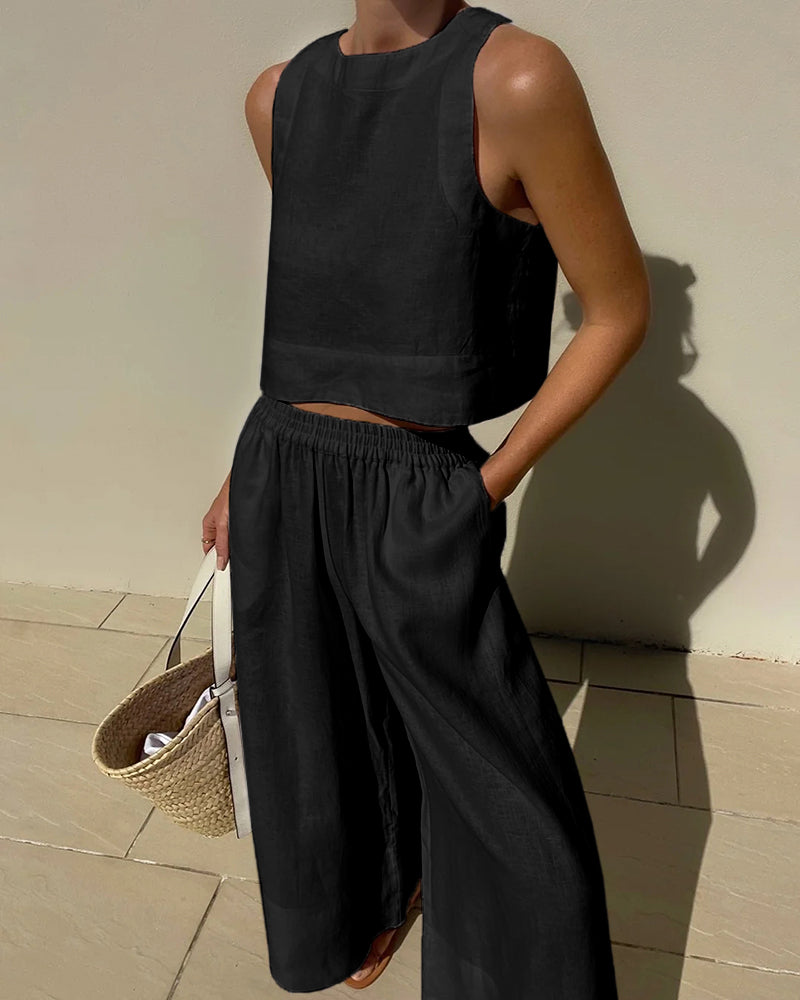 Frau in schwarzem Leinen-Zweiteiler mit Strohtasche, Sommermode, ärmelloses Top, weite Hose.