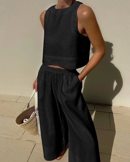Frau in schwarzem Leinen-Zweiteiler mit Strohtasche, Sommermode, ärmelloses Top, weite Hose.