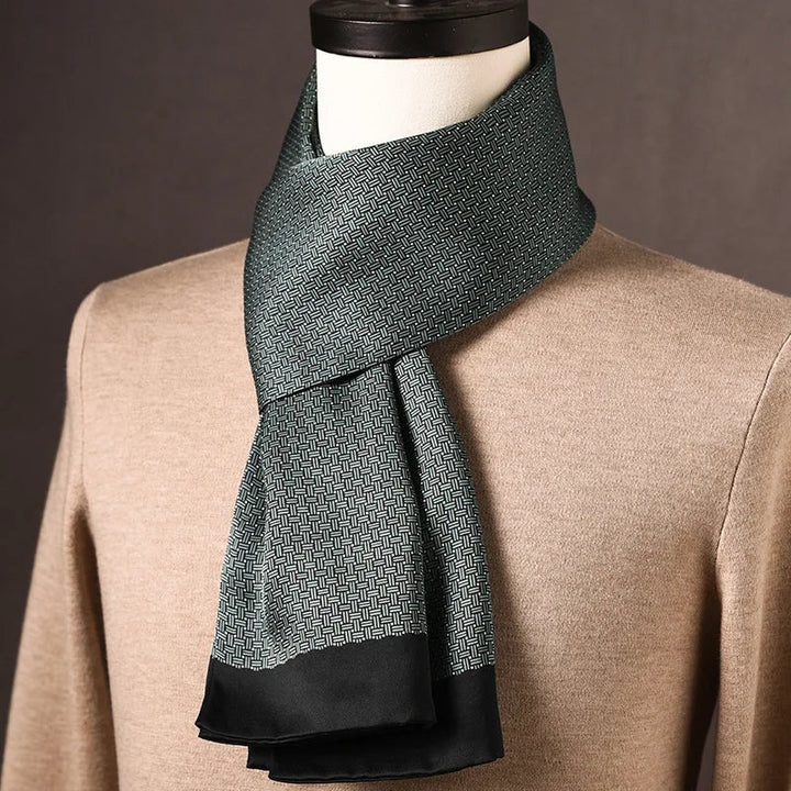 Grüner Schal mit feinem Flechtmuster und schwarzer Kante, locker um eine Büste über einem beigen Pullover gelegt. 23