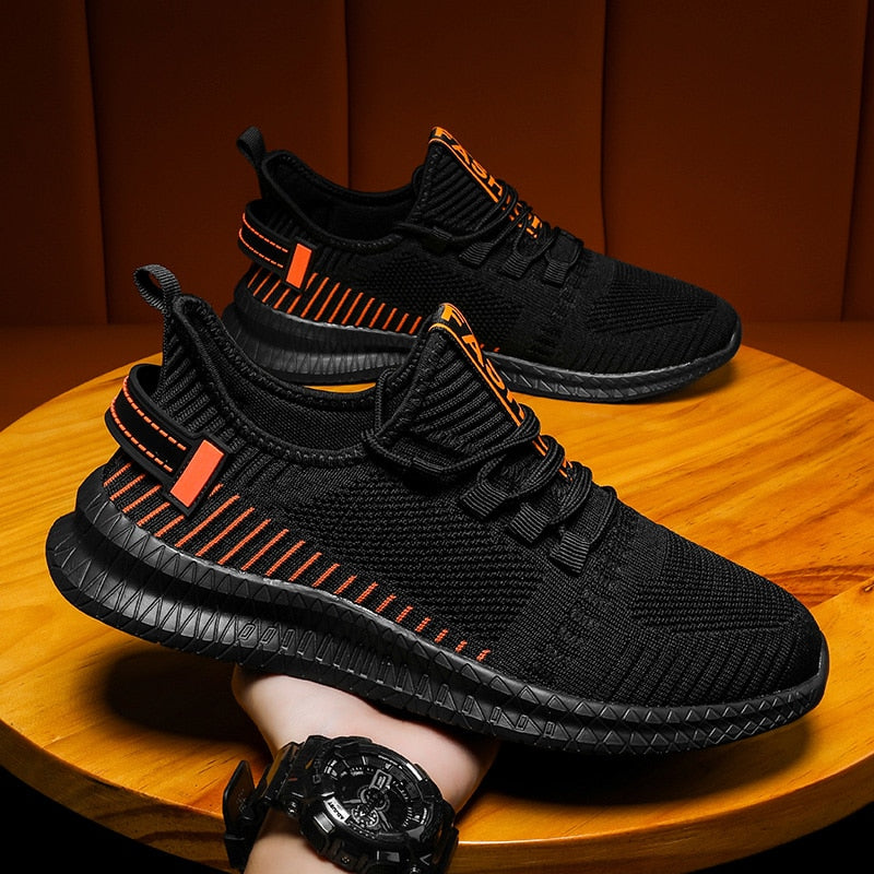 Schwarze Sportschuhe mit orangefarbenen Akzenten, atmungsaktives Mesh, rutschfeste Sohle.