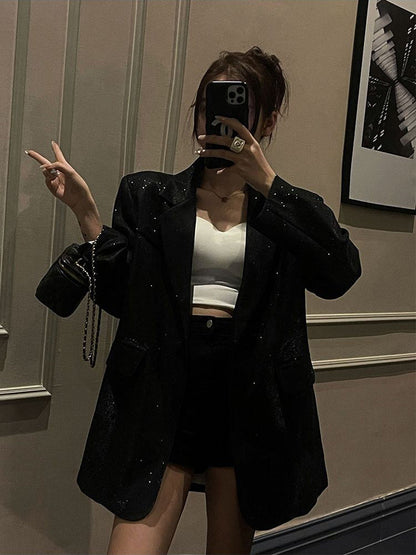 Frau in schwarzem Glitzerblazer, weißem Top, schwarzer Tasche, macht ein Selfie.