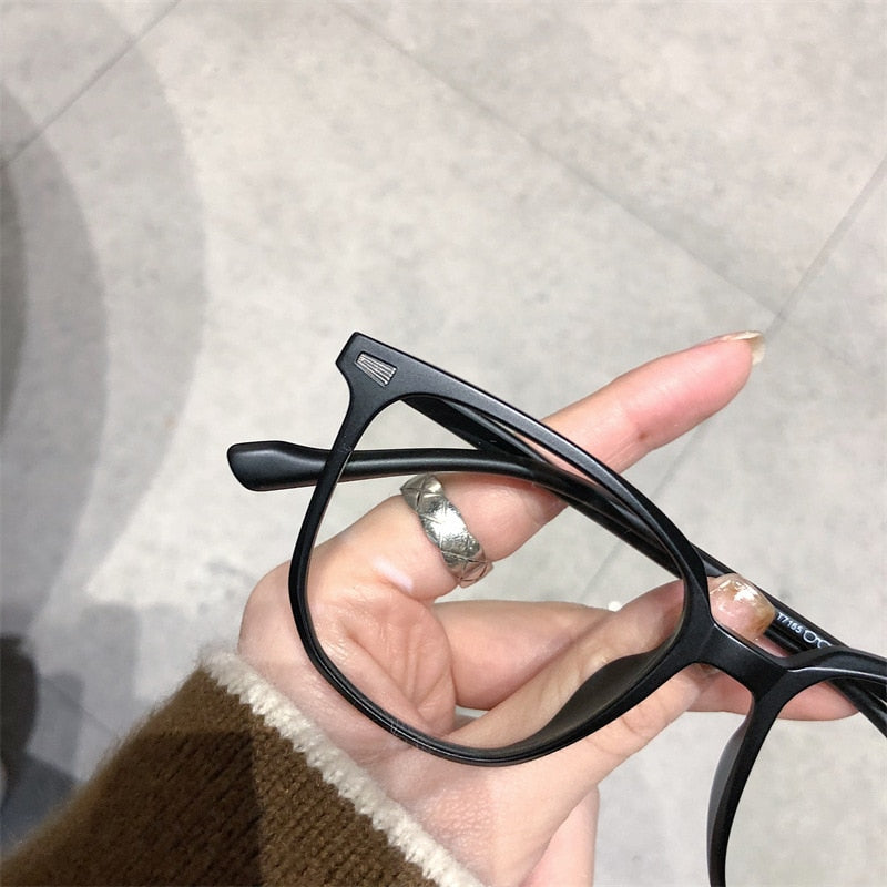 Schwarze Brille mit Kunststoffrahmen, rechteckig, in Hand gehalten, modisch, unisex.