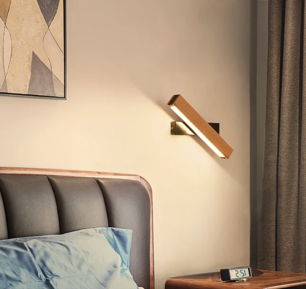 Wandlampe mit schwarzem Arm und gedrehter Holzleiste über einem gepolsterten Bett, daneben Vorhang und Digitaluhr. 8