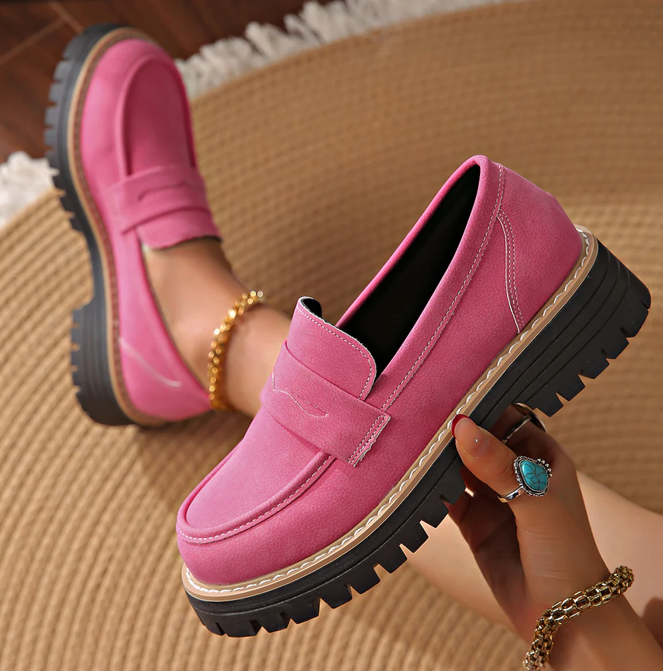 Pinke Loafer mit Plateausohle, ein Schuh wird in der Hand gehalten, Trägerin sitzt auf einem Jute-Teppich. 18