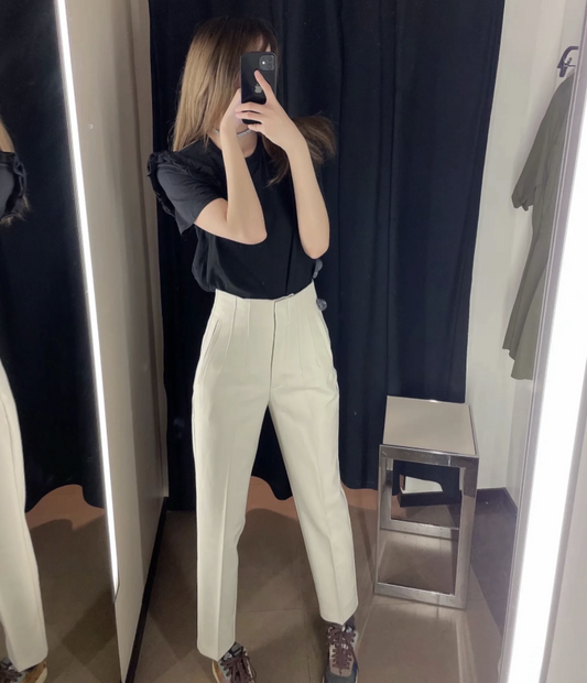 Frau in Umkleidekabine mit schwarzem Oberteil und weißen Hosen, Spiegel-Selfie, Mode.