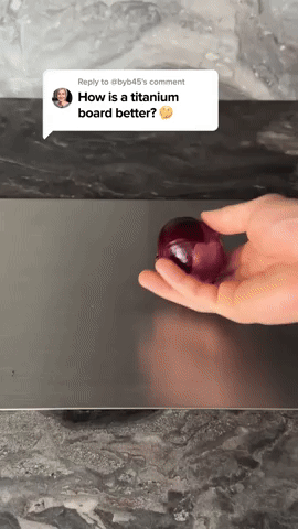 Hand rollt eine rote Zwiebel über die glatte, dunkle Metalloberfläche des Schneidebretts auf einer Marmorarbeitsplatte, Videostandbild mit Kommentarblase. 5
