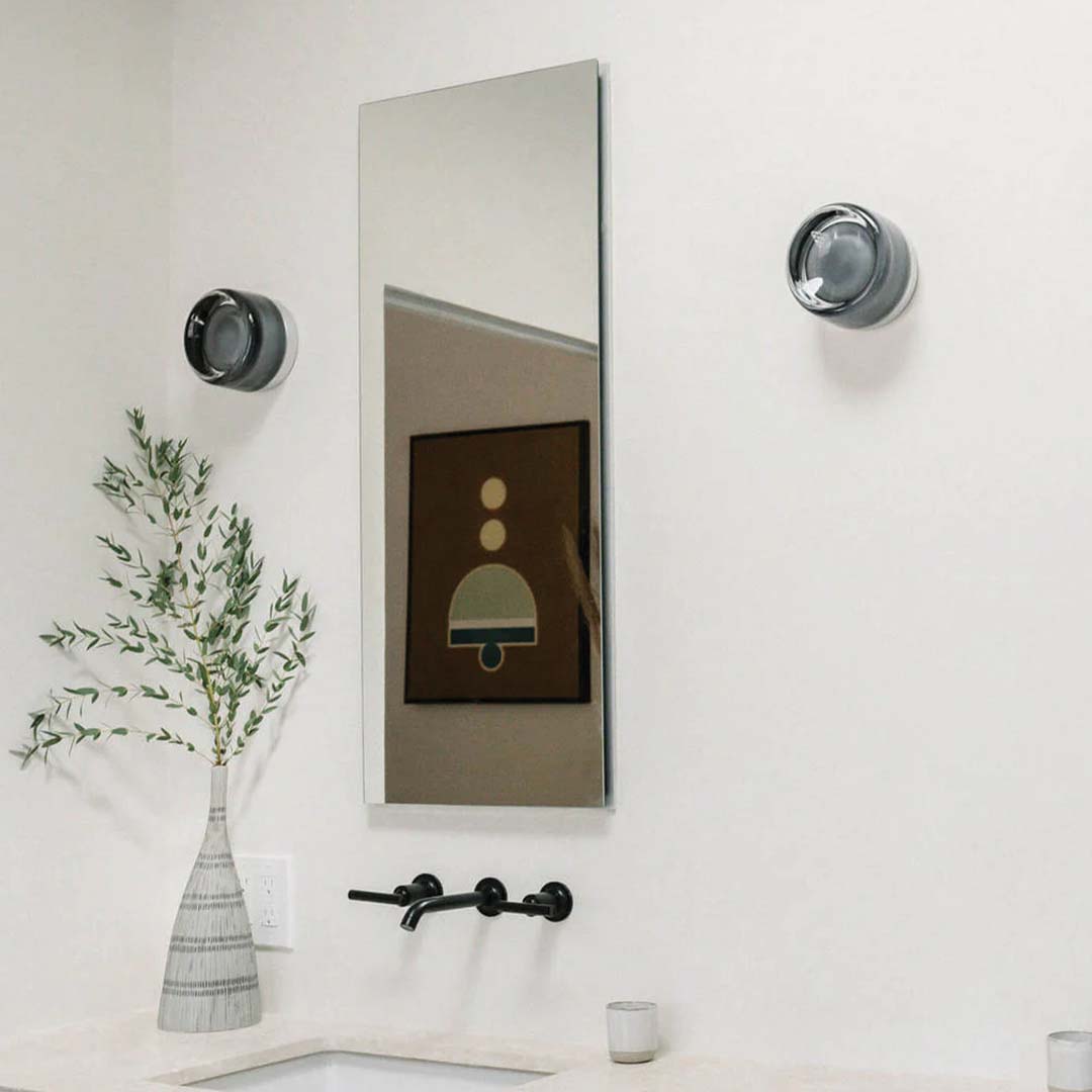 Moderner Badezimmer-Wandspiegel mit schwarzem Wasserhahn, Vase mit Zweigen, minimalistische Dekoration.