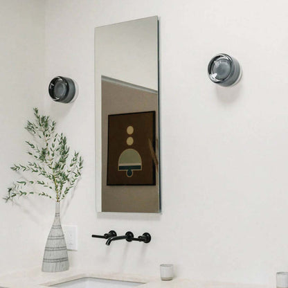 Moderner Badezimmer-Wandspiegel mit schwarzem Wasserhahn, Vase mit Zweigen, minimalistische Dekoration.