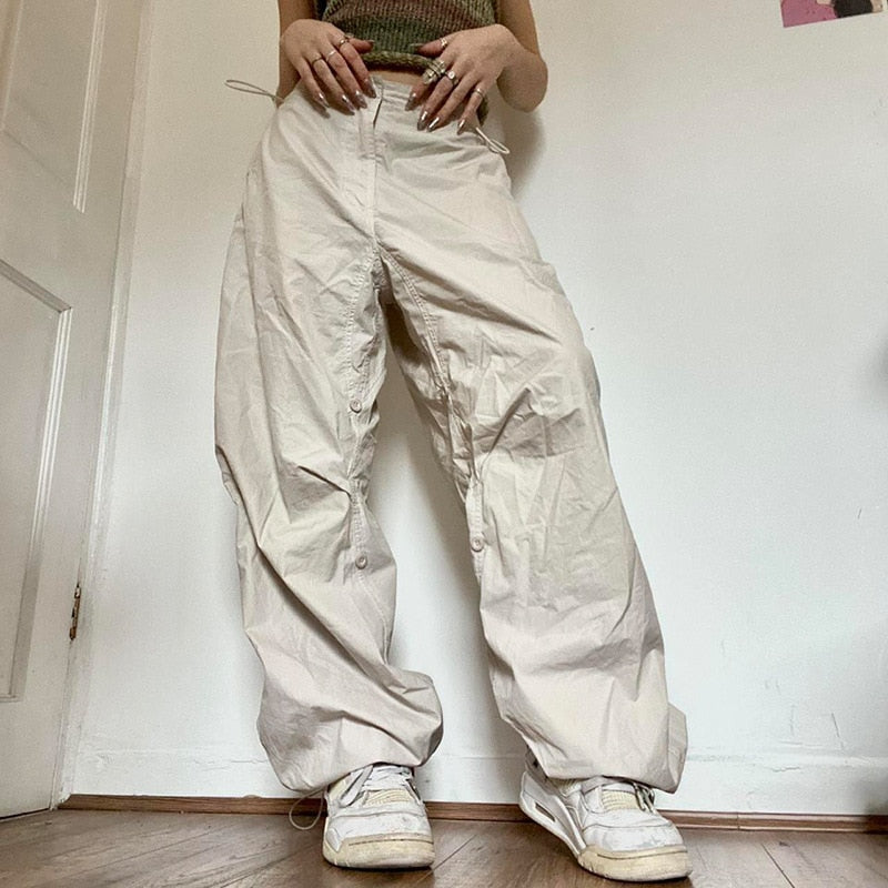 Frau trägt beige Baggy-Hose, weiße Sneaker, lässiger Stil, modische Damenbekleidung.