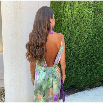 Frau im rückenfreien, bunten Sommerkleid vor Hecke, lange braune Haare, lila Ohrringe.