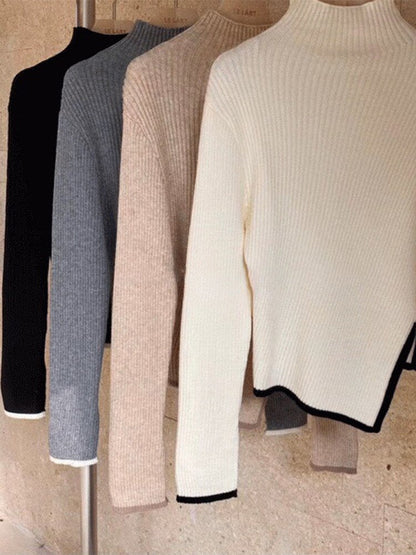 Vier Rollkragenpullover in Schwarz, Grau, Beige und Weiß aus Strickstoff auf Kleiderstange.