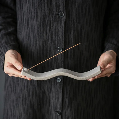 Person hält grauen Keramik-Räucherstäbchenhalter, wellenförmig, minimalistisch, modern.