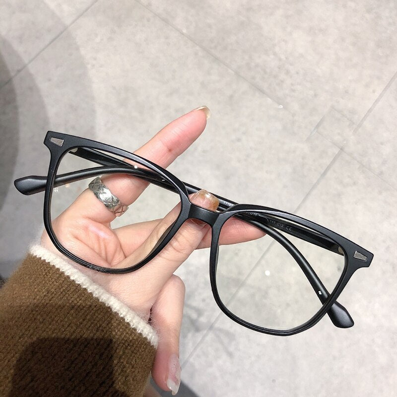 Schwarze Unisex-Brille, rechteckig, Kunststoffrahmen, modisch, auf grauem Hintergrund.