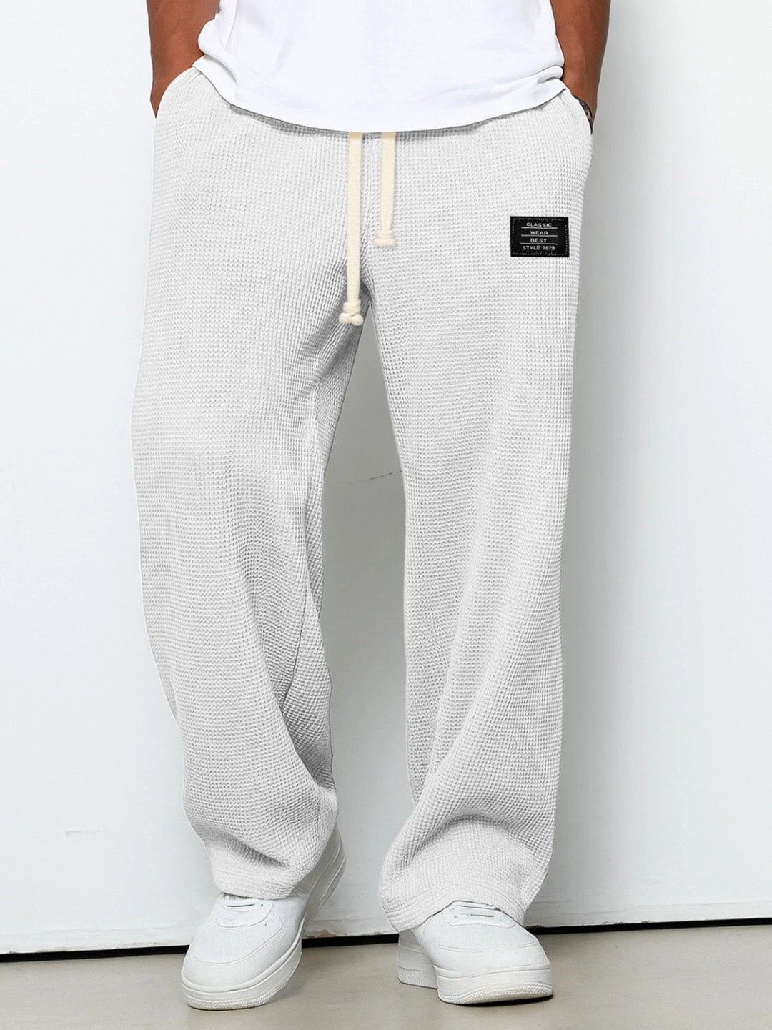 Dieselbe Waffelstrickhose in sehr hellem Grau, vor einer weißen Wand getragen, mit Kordelzug am elastischen Bund. 2