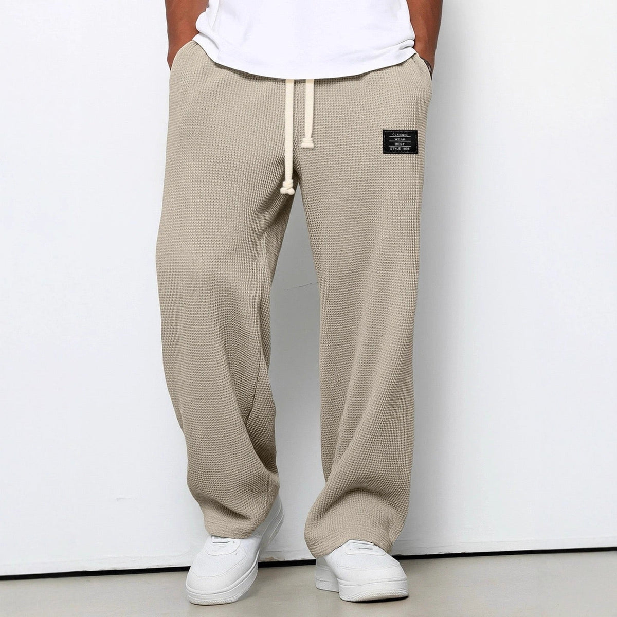 Waffelstrickhose in Beige, Frontansicht am Model mit weißem T-Shirt und Sneakern, Hände in den Taschen. 6