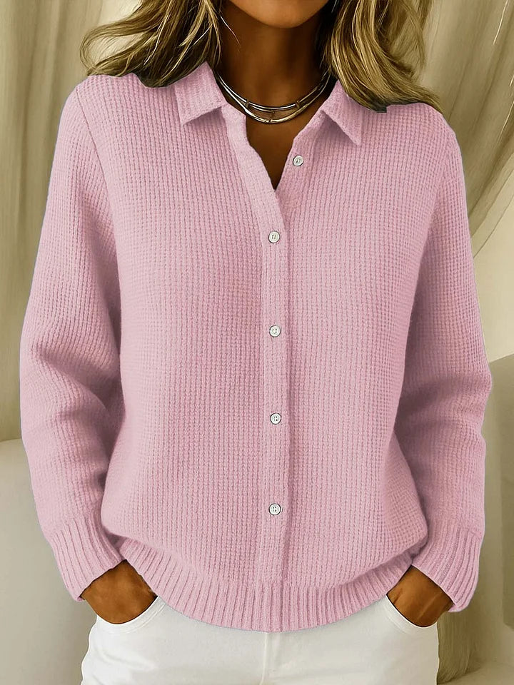 Frontansicht des Strickpullovers in Rosa mit Waffelstruktur, Kragen und Knopfleiste, getragen zu weißer Hose und Silberkette. 2