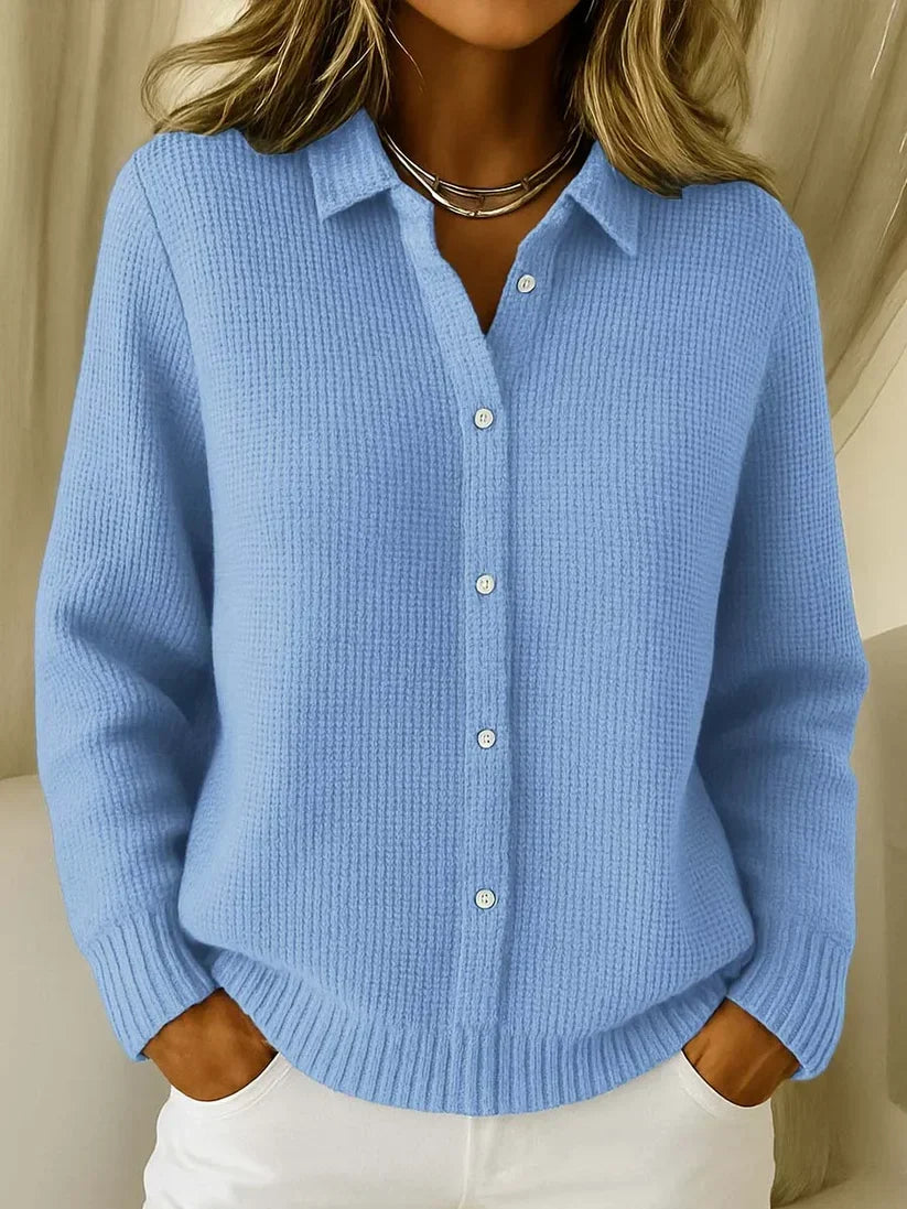 Frau trägt den Strickpullover in Hellblau mit Kragen und Knopfleiste, Hände in den Taschen einer weißen Hose, Frontansicht. 1
