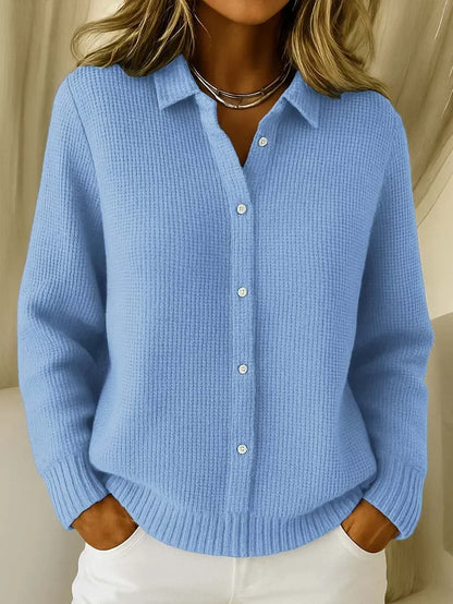 Frau trägt den Strickpullover in Hellblau mit Kragen und Knopfleiste, Hände in den Taschen einer weißen Hose, Frontansicht. 1