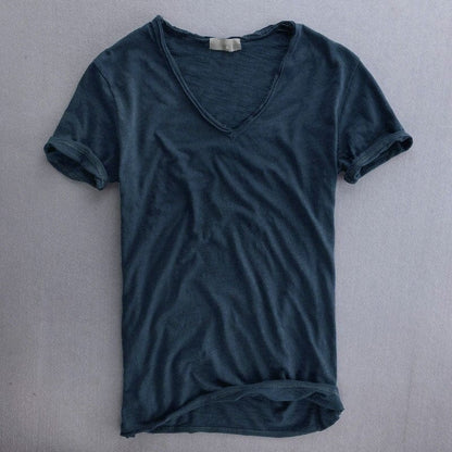 T-Shirt in dunklem Blaugrau mit tiefem V-Ausschnitt und umgeschlagenen Ärmelsäumen, Vorderansicht flach auf grauem Untergrund. 5