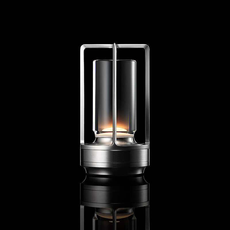 Studio-Aufnahme der leuchtenden Tischlampe in Silber-Optik mit Glaszylinder und offenem Rahmen vor schwarzem Hintergrund. 10