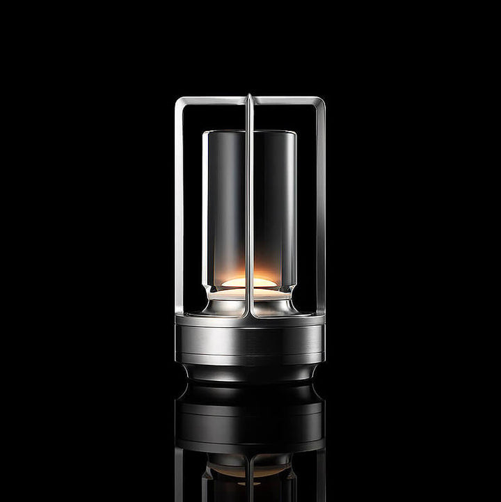 Studio-Aufnahme der leuchtenden Tischlampe in Silber-Optik mit Glaszylinder und offenem Rahmen vor schwarzem Hintergrund. 10