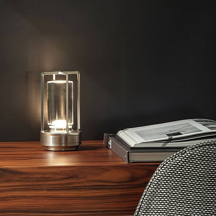 Silberfarbene Tischlampe leuchtet auf einem Holzsideboard neben aufgeschlagenen Büchern vor einer dunklen Wand. 5