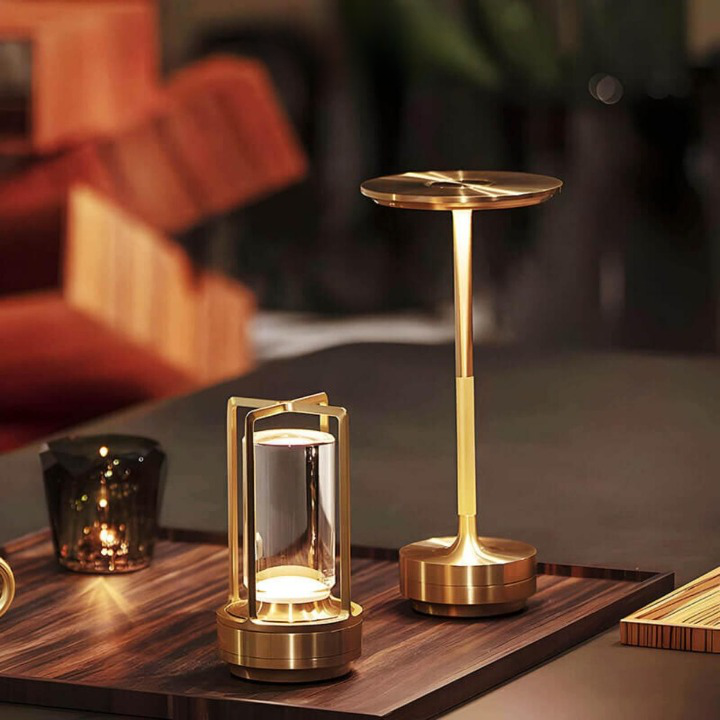 Messingfarbene Lampe mit Rahmenschirm steht neben einer schlanken Messing-Tischleuchte mit Tellerschirm auf einem Holztablett. 7