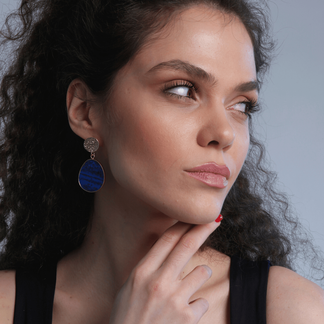 Frau mit blauen Ohrringen, lockigem Haar, schwarzem Top, nachdenklicher Blick.