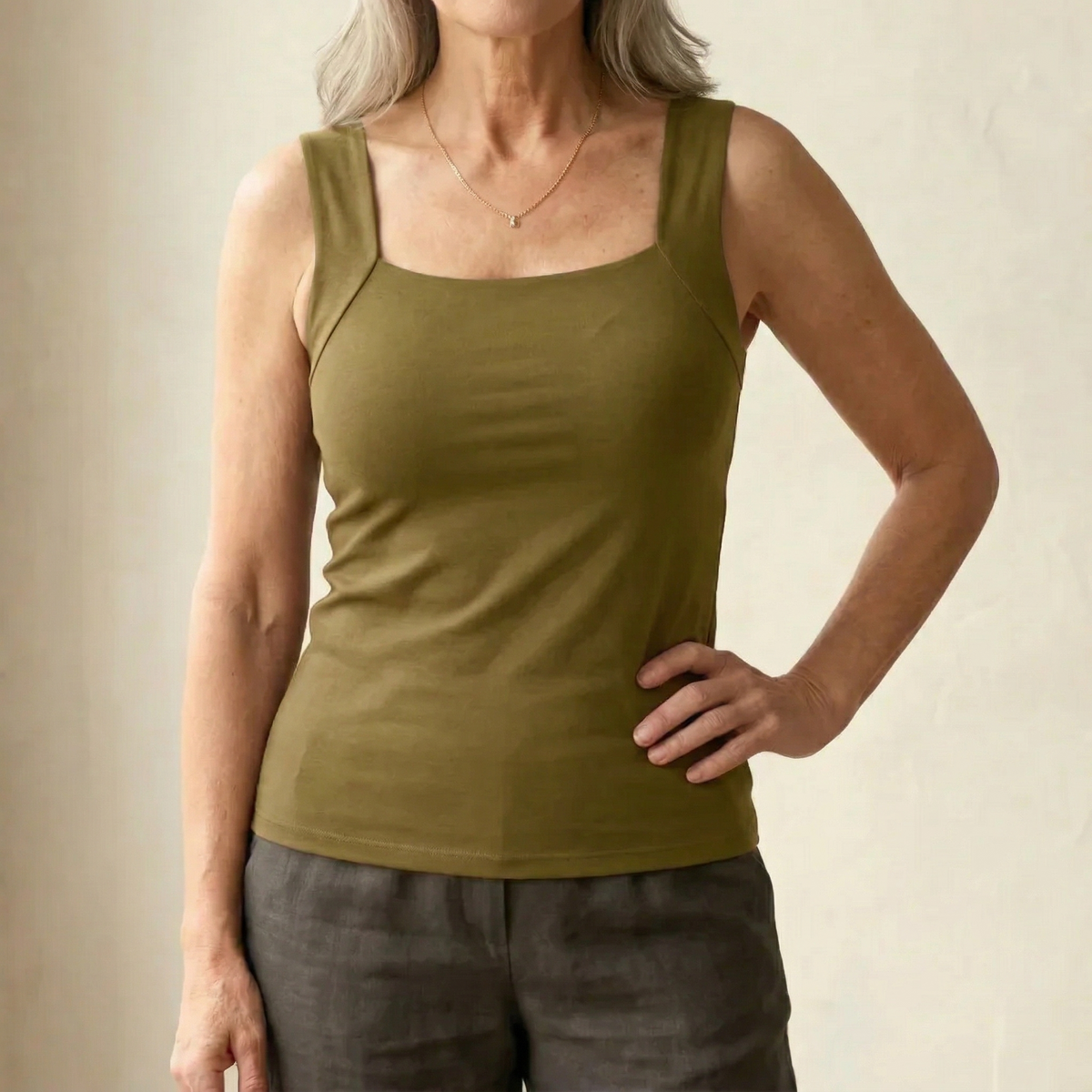 Frau im olivgrünen Tanktop mit breiten Trägern, mit feiner Halskette und grauer Leinenhose, Hand an der Hüfte. 14