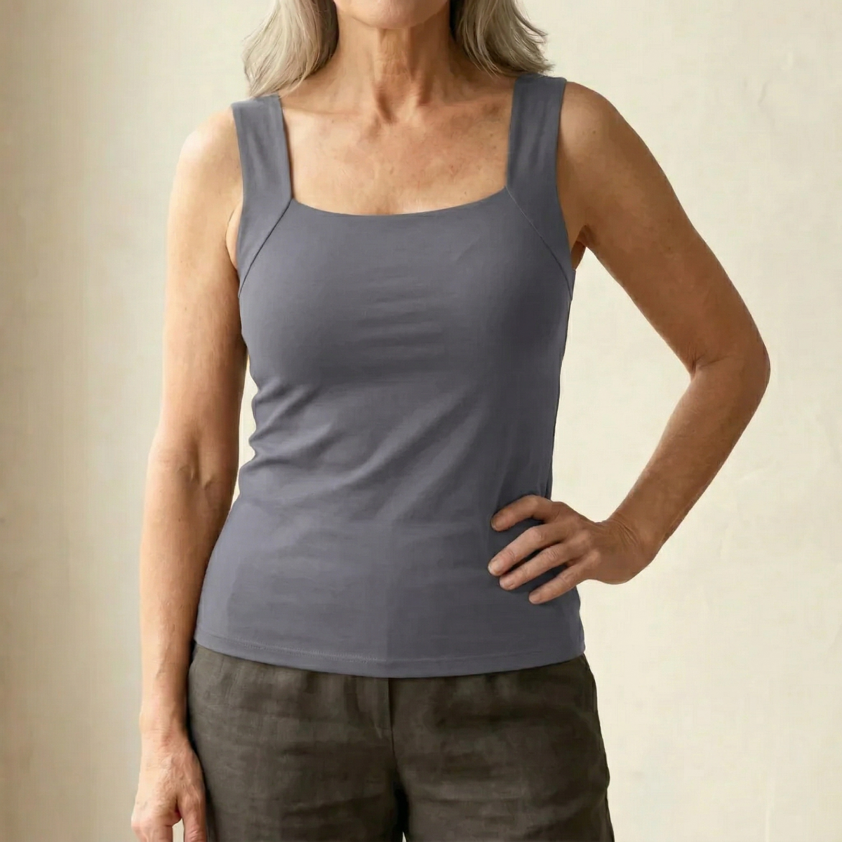 Frau im grauen Tanktop mit eckigem Ausschnitt und breiten Trägern, dazu eine Leinenhose, eine Hand an der Hüfte. 15