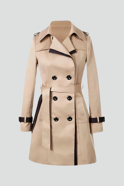 Beiger zweireihiger Trenchcoat mit dunklen Zierkanten, Bindegürtel und Ärmelriemen, frei gestellt auf hellem Hintergrund. 1
