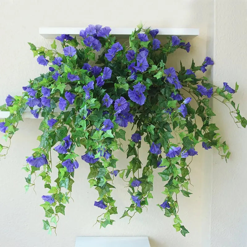 Blauviolette Kunstblumen mit langen, herabfallenden Ranken auf einem weißen Wandregal vor heller Wand. 4