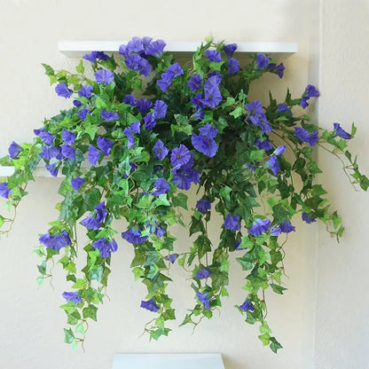 Blauviolette Kunstblumen mit langen, herabfallenden Ranken auf einem weißen Wandregal vor heller Wand. 4