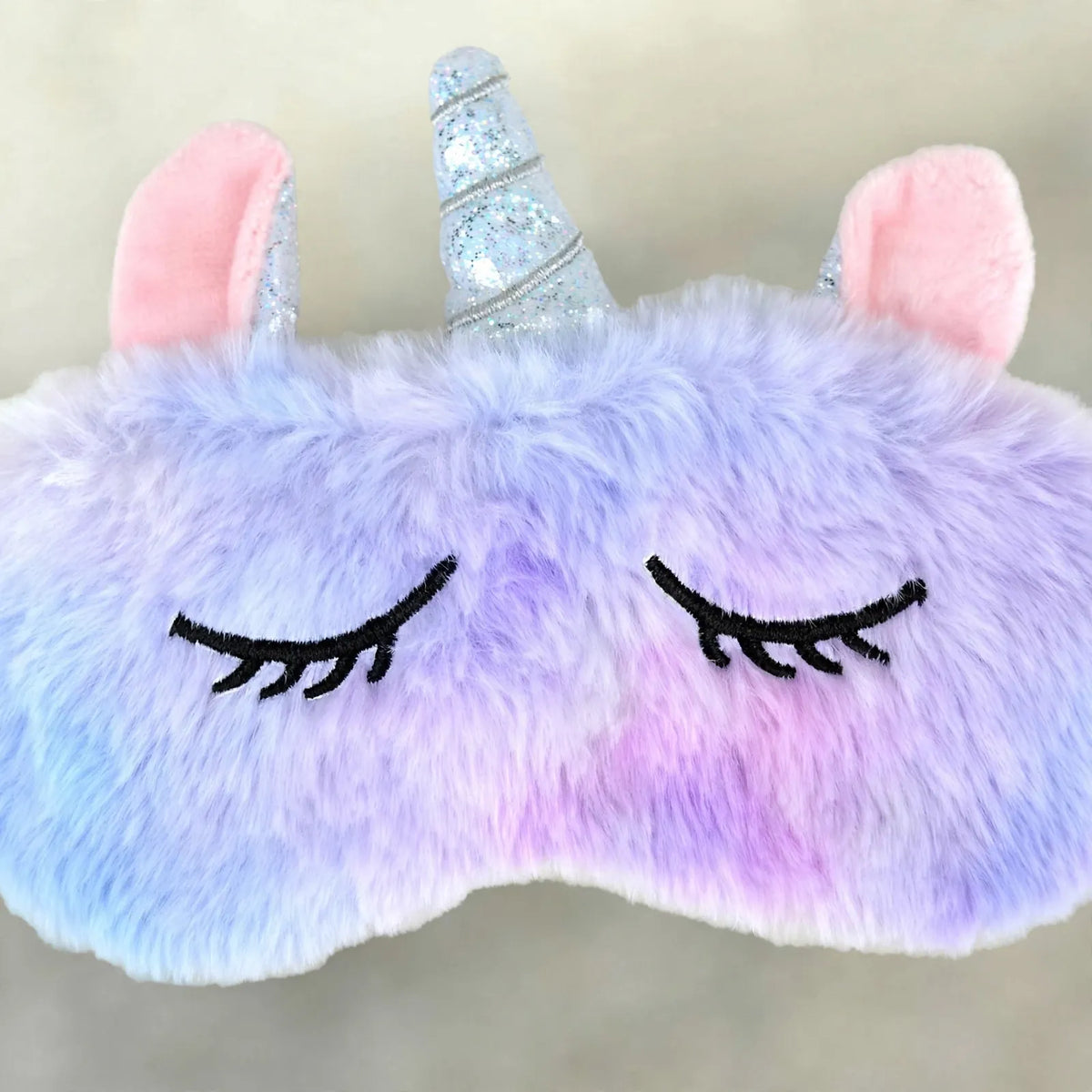 Nahaufnahme der flauschigen Einhorn-Schlafmaske in Lila und Rosa mit Glitzerhorn und gestickten Wimpern 3
