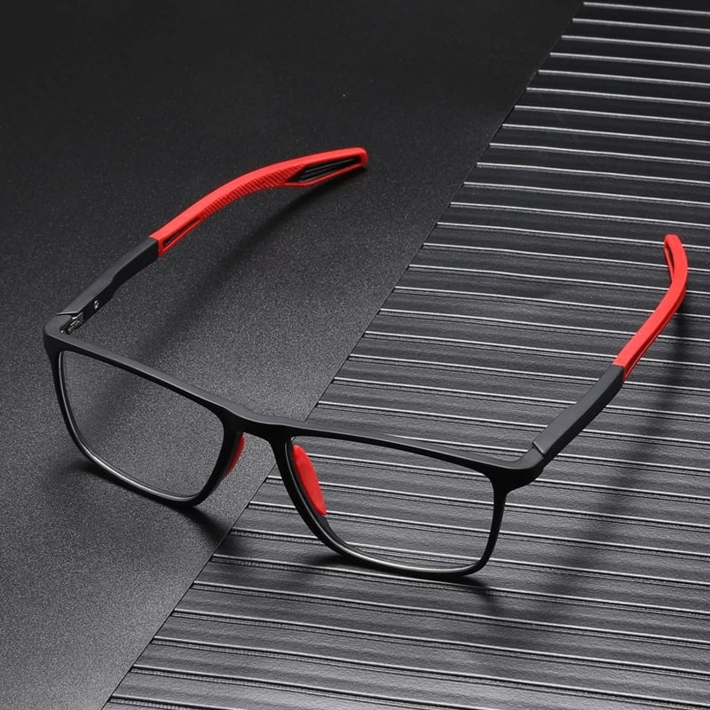 Schwarze Brille mit roten Bügelenden und roten Nasenpads, auf dunkler gerillter Unterlage liegend 3